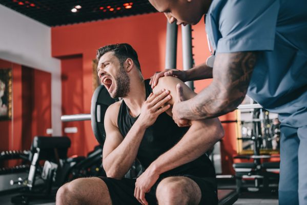 medico-afroamericano-tocando-hombro-lesionado-mal-tecnica-en el-gimnasio-de-sus-ejercicios